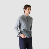 Front view: A person holds the Navy Blue CLUTCH IN CACHEMIRE LEATHER AND MOSAICO with wrist strap in the left hand, carried elegantly in front of the body.