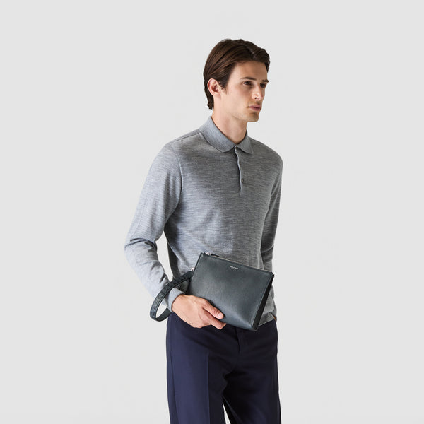 Front view: A person holds the Navy Blue CLUTCH IN CACHEMIRE LEATHER AND MOSAICO with wrist strap in the left hand, carried elegantly in front of the body.