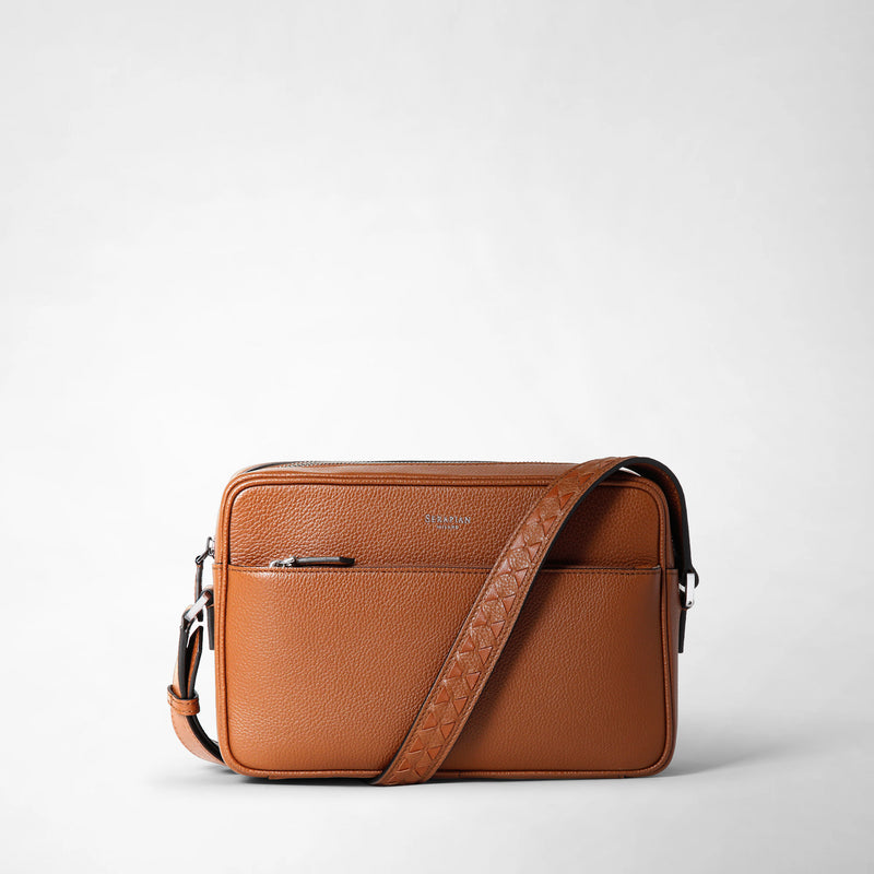 Frontal view: EAST WEST CROSSBODY BAG IN CACHEMIRE LEATHER shows a compact, rectangular tobacco-colored leather crossbody bag with a textured surface, front zipper pocket, and adjustable strap.