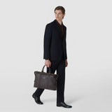 Front view: A man carries the SOFT BRIEFCASE IN CACHEMIRE LEATHER AND MOSAICO in espresso-colored leather, featuring double handles and decorative Mosaico strips, against a neutral background.