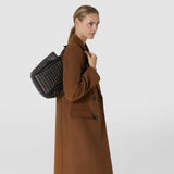 Side view: A woman carries the BUCKET IN MOSAICO MESTIERI D'ARTE over her shoulder; the black leather bag features a three-color woven mosaic pattern.