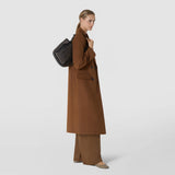 Side view: A woman wears the BUCKET IN MOSAICO MESTIERI D'ARTE over her shoulder; the dark brown bucket bag features an intricate, multicolored leather weave against a light studio background.