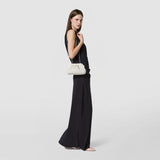 Front view: MINI SECRET CLUTCH BAG IN MOSAICO MICROCHAIN hangs from a fine chain over a woman's shoulder. The cream-colored bag features a woven Mosaico pattern against a black dress.