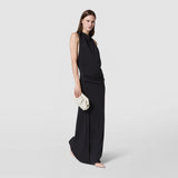 Front view: A woman holds the cream-colored MINI SECRET CLUTCH BAG IN MOSAICO MICROCHAIN beside a long black dress; the woven Mosaico pattern is clearly visible.