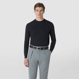Front view: A man wears the black BELT IN MOSAICO with a geometric woven pattern and silver buckle, paired with light gray trousers and a dark sweater against a light background.