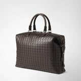 Detail view: BRIEFCASE IN MOSAICO is shown against a light background; the dark brown briefcase features a woven leather pattern, two handles, metal hardware, and a zipper.