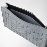 Detail view: CLUTCH IN MOSAICO lies open, showing Arctic Blue geometrically woven leather, a silver zipper, and dark lining. Visible lettering: “SERAPIAN,” “MADE IN ITALY.”