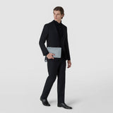 Front view: A man in a black suit holds the CLUTCH IN MOSAICO, made of Arctic Blue woven leather with a zipper and wrist strap, in front of him.