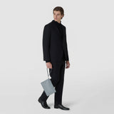 CLUTCH IN MOSAICO in ice-blue, geometrically woven leather with a wrist strap; a man carries it in his hand. Front view against a light, neutral background.