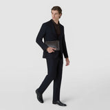 Front view: An elegantly dressed man holds the CLUTCH IN MOSAICO, made of dark blue woven leather with a zipper and wrist strap, in front of his body; the “SERAPIAN” lettering is visible.