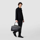 Front view of a man carrying the TRAVEL BAG IN MOSAICO in Chiaroscuro Mosaico nappa leather in black and white with woven pattern and two handles.