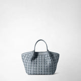 Front view: MINI SECRET BAG IN RIBBON MOSAICO stands against a light background; the ice-blue handbag features a three-dimensional woven pattern, two short handles, and the embossed lettering “SERAPIAN MILANO”.