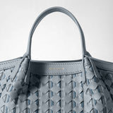 Detail view: MINI SECRET BAG IN RIBBON MOSAICO shows its ice-blue, three-dimensional woven leather body and handle, with gold-tone “SERAPIAN MILANO” embossing against a light background.