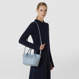 Front view: A woman carries the MINI SECRET BAG IN RIBBON MOSAICO in ice blue, featuring a three-dimensional woven texture, short handles, and a long shoulder strap.