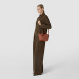 Front view: A woman carries the MINI SECRET BAG IN MOSAICO by its short handle and long shoulder strap; the brick-red woven leather is clearly visible.