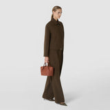 Front view: MINI SECRET BAG IN MOSAICO hangs from the hand of an elegantly dressed woman. The compact, brick-red top-handle bag displays its woven Mosaico leather texture against a light studio background.