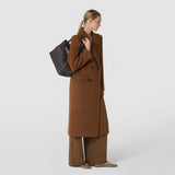 Side view: A woman carries the SMALL SECRET TOTE BAG IN RIBBON MOSAICO over her shoulder; the dark brown bag features a textured woven leather finish.
