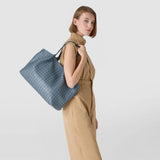 側面図、女性が肩にMOSAICO製SECRETトートバッグを掛けている。インディゴカラーの編み込みナッパレザー、グラフィックなMOSAICO柄、大きく柔らかで収納力のあるフォルム。