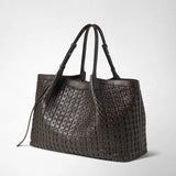 Detail view: SECRET TOTE BAG IN RIBBON MOSAICO stands at an angle against a light background; dark brown leather with a woven texture, long handles, and the “SERAPIAN MILANO” embossing are visible.