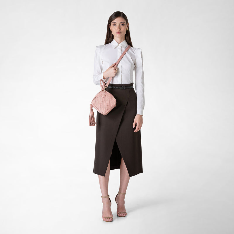 Vista frontale di una donna in piedi che indossa la PETRA HANDBAG IN MOSAICO color blush a tracolla, con nappina laterale, su sfondo neutro.