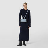 Front view: A woman wears the MINI ANI BAG IN RIBBON MOSAICO as a light blue textured shoulder bag against a light background, paired with a navy knit dress.