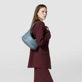 Side view: Model carries the SMALL ANI SHOULDER BAG IN MOSAICO in Storm, a compact, light blue shoulder bag with distinctive woven pattern on the arm.