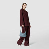 Side view of a woman in a burgundy pantsuit casually holding the SMALL ANI SHOULDER BAG IN MOSAICO Storm in her right hand.