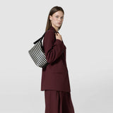 Side view: SMALL ANI SHOULDER BAG IN MOSAICO carried on the shoulder, displaying a black and off-white geometric patterned woven leather bag with a black strap.