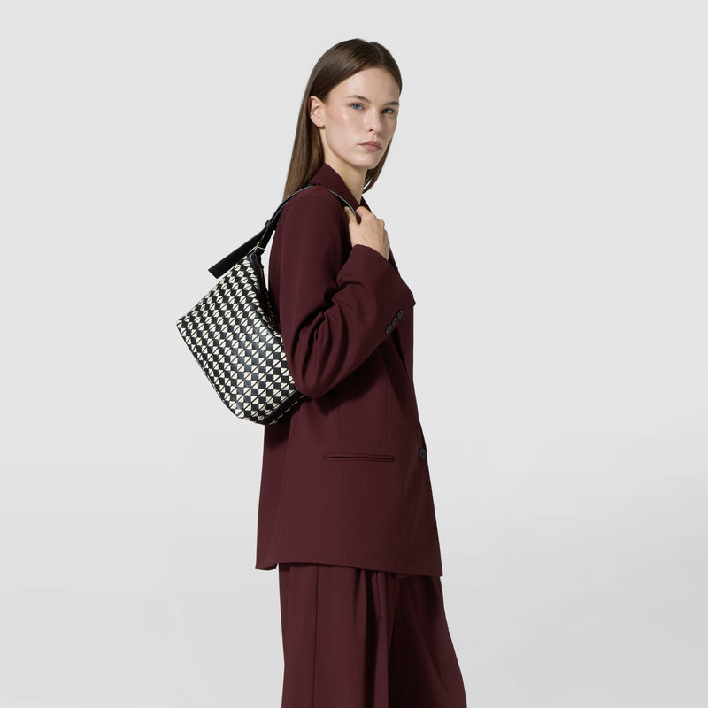 Side view: SMALL ANI SHOULDER BAG IN MOSAICO carried on the shoulder, displaying a black and off-white geometric patterned woven leather bag with a black strap.