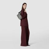 Side view: SMALL ANI SHOULDER BAG IN MOSAICO displayed on a model’s shoulder, showing a compact black and off-white woven leather bag against a plain background.