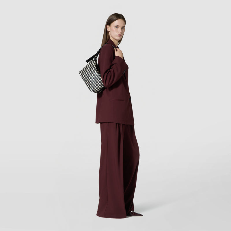 Side view: SMALL ANI SHOULDER BAG IN MOSAICO displayed on a model’s shoulder, showing a compact black and off-white woven leather bag against a plain background.