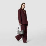 Frontal view: SMALL ANI SHOULDER BAG IN MOSAICO shown being carried by a woman wearing a burgundy suit, highlighting its black and off-white woven leather pattern and short shoulder strap.
