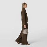 Side view: A woman carries the MINI BUCKET IN MOSAICO by hand; the beige bag features a woven mosaic pattern, short handles, and side straps.