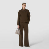 Front view: A woman carries the MINI BUCKET IN MOSAICO by its short handles. The compact Sahara beige bag features an embossed Mosaico pattern and a plaque reading “SERAPIAN.”