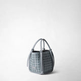 Angled view: MINI BUCKET IN RIBBON MOSAICO is shown open against a light background; icy blue, three-dimensional woven leather, soft bucket shape, slim handles, and the SERAPIAN logo are visible.
