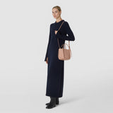 Front view: A woman wears the MINI BUCKET IN MOSAICO in Sandalwood Pink over her shoulder; the compact bag features embossed Mosaico leather and narrow straps.