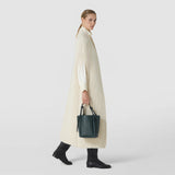 Front view: BUCKET IN RIBBON MOSAICO hangs from a model’s hand; the forest green bag features a textured woven surface, two handles, and a soft bucket shape.