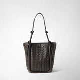 Vista frontale: BUCKET IN MOSAICO RIBBON è davanti a uno sfondo chiaro; la borsa in pelle color ebano presenta una struttura intrecciata tridimensionale e lunghi spallacci.