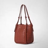 BUCKET IN MOSAICO shown in close-up with brick-red, geometrically woven leather, long shoulder straps, and small knot details against a light background.
