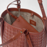 Detail view: BUCKET IN MOSAICO shows brick-red woven leather, a shoulder strap, and a light suede interior compartment. The label reads “SERAPIAN MILANO MADE IN ITALY”.