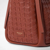 Detail view: BUCKET IN MOSAICO features brick-red, geometrically woven Mosaico leather, a wide leather strap, and a brand label reading “SERAPIAN MILANO”.