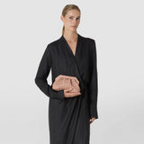 Front view: A woman holds the MINI SECRET CLUTCH BAG IN MOSAICO in front of her body. The small sandal-colored clutch features a woven diamond pattern and a light-colored frame.