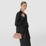 Front view: A woman wears the MINI SECRET CLUTCH BAG IN MOSAICO as a crossbody bag. The sandal-colored clutch with a geometric mosaic pattern hangs from a fine gold-tone chain.