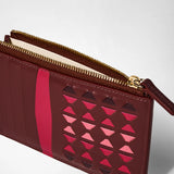 Detail view: ZIP CARD CASE IN MOSAICO made of rosewood leather, features intricate handwoven pink and red geometric patterns, several card slots, and a gold zippered pocket.