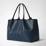 Front view: SECRET TOTE BAG IN STEPAN stands in a studio; the ocean blue bag with an embossed pattern, navy leather details, and long handles bears the “SERAPIAN MILANO” logo.