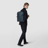 Side view: A man wears the BACKPACK IN STEPAN in ocean blue; its textured front with a zipper, front pocket, and side strap is shown against a light background.