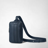 Detail view: SLING BACKPACK IN STEPAN is shown with a long shoulder strap against a light background; navy surface with an embossed pattern, zipper, and “SERAPIAN MILANO” lettering.