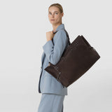 Front view: A woman wears the MAXI MARO BAG IN SUEDE AND MOSAICO over her shoulder. The large dark brown bag features woven Mosaico panels and knotted leather details against a light background.