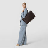 Side view: A woman carries the MAXI MARO BAG IN SUEDE AND MOSAICO over her shoulder; the spacious dark brown bag features woven Mosaico details against a light background.
