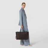 Front view: A woman carries the MAXI MARO BAG IN SUEDE AND MOSAICO; the spacious dark brown bag features woven Mosaico panels, long handles, and side leather strips against a light background.